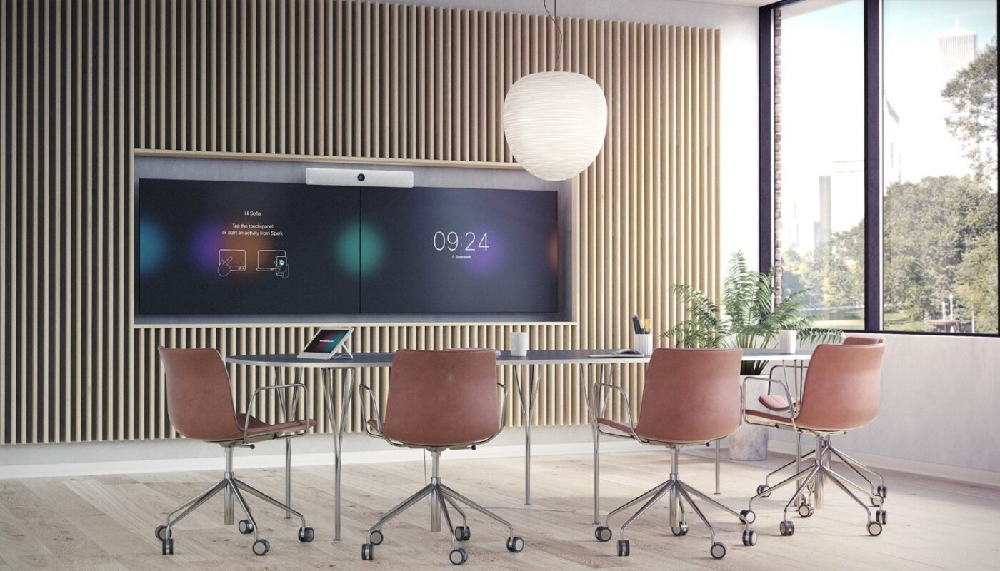 Modernt konferensrum med fem bruna snurrfåtöljer runt ett bord, en stor väggmonterad skärm med digital klocka och Cisco Webex-gränssnitt samt en stor taklampa.