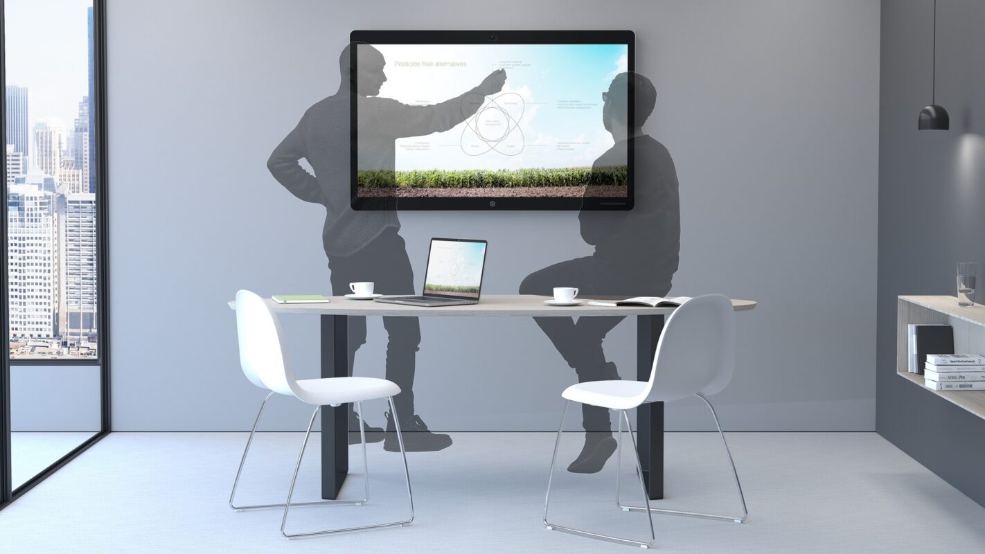 Ett modernt kontorsrum med två tomma vita stolar, ett bord med en bärbar dator och kaffekoppar samt en väggmonterad skärm som visar ett Cisco Webex-diagram; stadsbilden syns genom fönstret.