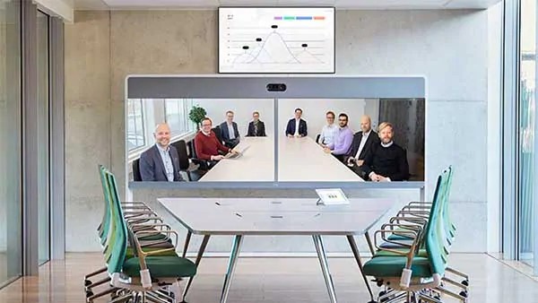 Ett modernt konferensrum med gröna stolar och en stor skärm som visar ett virtuellt Cisco Webex-möte med åtta personer och ett diagram som visas ovanför skärmen.