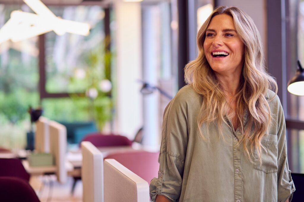 Mature Businesswoman Standing By Partition In Open Plan Office