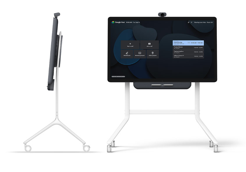 En stor digital skärm på ett hjulförsett stativ visas framifrån och från sidan; skärmen visar ett Google Meet-gränssnitt för videokonferenser.
