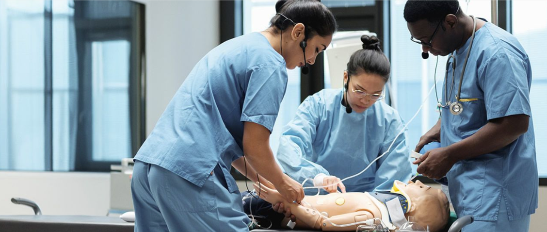 Tre läkare i operationskläder övar ett ingrepp på en medicinsk simuleringsdocka på Kliniska träningscenter i en klinisk utbildningsmiljö.