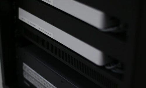 En närbild av ett serverrack med två vita nätverksenheter och en svart kontrollpanel med knappar och indikatorlampor, som visar moderna lösningar för effektiv nätverkshantering. En närbild av ett serverrack med två vita nätverksenheter och en svart kontrollpanel med knappar och indikatorlampor, som visar moderna lösningar för effektiv nätverkshantering.